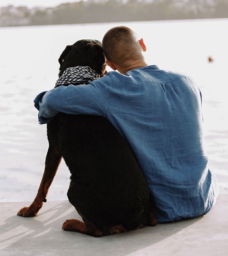 man wearing a blue shirt hugging his rottweiler dog